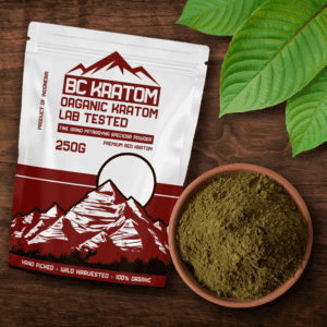 Red BC Kratom bag laying on a wooden table next to a bowl of Red Kapuas Kratom Powder