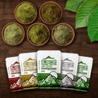 Five BC Kratom 25g sample bags laying on a wooden table beside five bowls of kratom powder